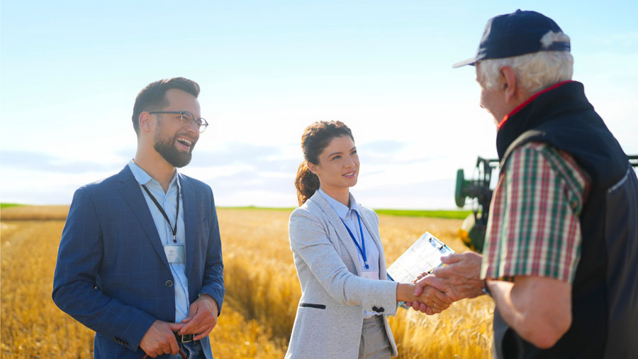 2Geschäftsleute reden mit einem Landwirt direkt auf einem Feld.