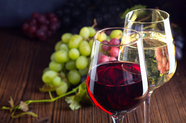Zwei Weingläser mit Rot- und Weißwein und Weintrauben.