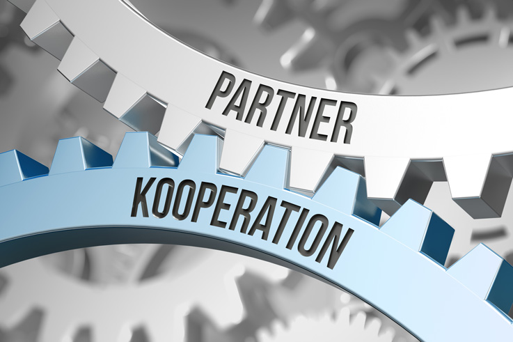 Zwei Zahnräder mit der Aufschrift "Partner, Kooperation" greifen ineinander.