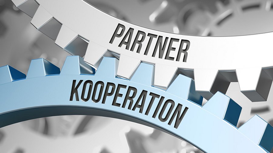 Zwei Zahnräder mit der Aufschrift "Partner, Kooperation" greifen ineinander.
