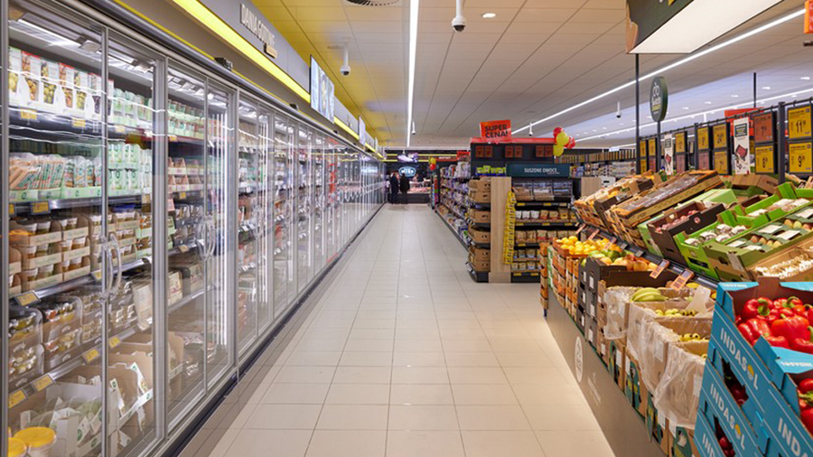 Einblick in einen Supermarktgang, Kühlregale und Obst-Gemüse-Abteilung.