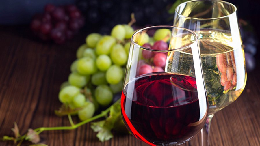 Zwei Weingläser mit Rot- und Weißwein und Weintrauben.